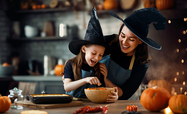  smiling mom and daughter in witch hat making food for Halloween