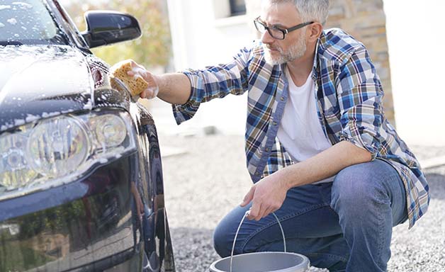 Mature man washing his car with soapy sponge in driveway