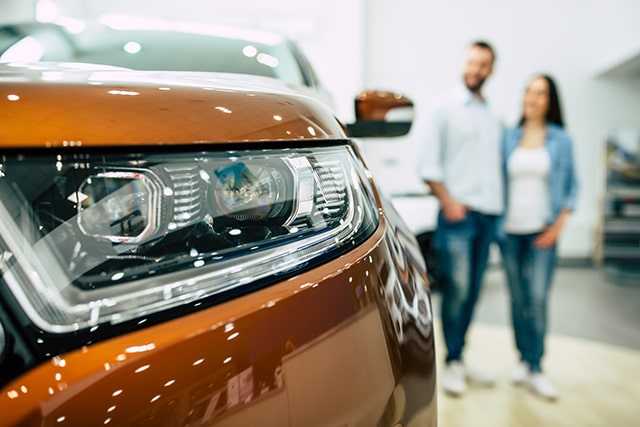 Couple buying new orange car in showroom