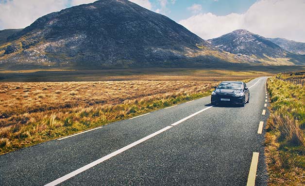 Car driving on empty scenic road trough nature by the lough inagh with mountains in the background